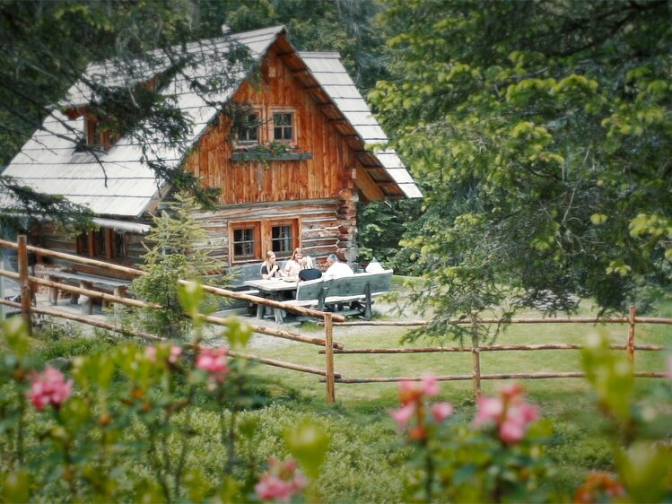 Rustic wooden cabin nestled in lush greenery, with a charming porch and surrounded by blooming flowers.