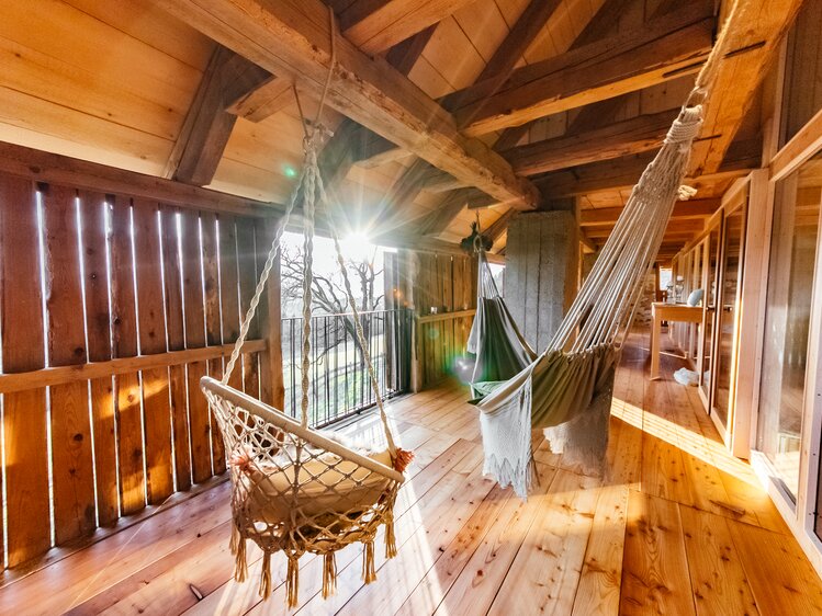 Cozy wooden cabin with hammocks, rustic furniture, and string lighting creating a peaceful, nature-inspired ambiance. | © Urlaub am Bauernhof Kärnten / Daniel Gollner