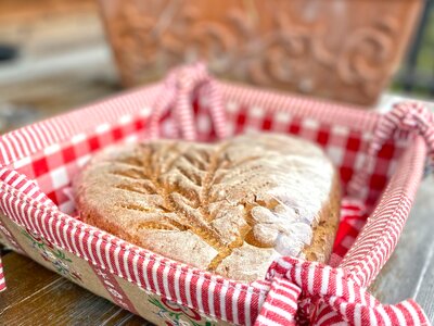 Rustic wooden box with loaf of bread, red-and-white striped napkin, and potted flowers in background. | © Urlaub am Bauernhof Kärnten / Jasmin Kreulitsch