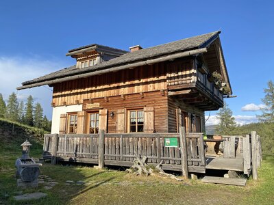 Rustic wooden mountain cabin with balcony, surrounded by lush greenery and blue sky. | © Urlaub am Bauernhof Kärnten / Jasmin Kreulitsch