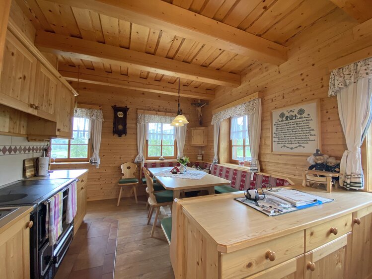 Cozy rustic wooden cabin interior with kitchenette, dining area, and wall decor. Warm, inviting atmosphere with traditional furnishings. | © Urlaub am Bauernhof Kärnten / Jasmin Kreulitsch