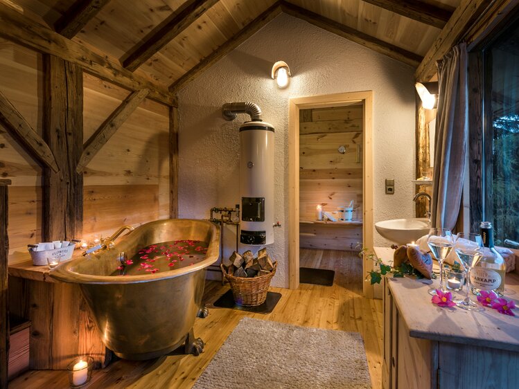 Cozy wooden cabin interior with copper bathtub, fireplace, and relaxing ambiance. Candles, wooden beams, and natural decor create a warm and inviting atmosphere. | © Günter Standl 