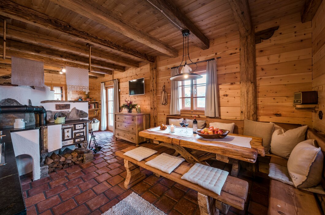 Cozy wooden cabin interior with rustic furnishings, fireplace, and dining area displaying fruits and flowers. | © Günter Standl 