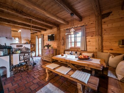 Cozy wooden cabin interior with rustic furnishings, fireplace, and dining area displaying fruits and flowers. | © Günter Standl 