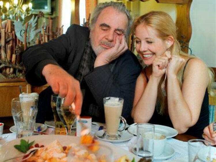 Middle-aged man and young woman enjoying drinks and dessert in rustic cafe setting, smiling companionably. | © Urlaub am Bauernhof / Schell
