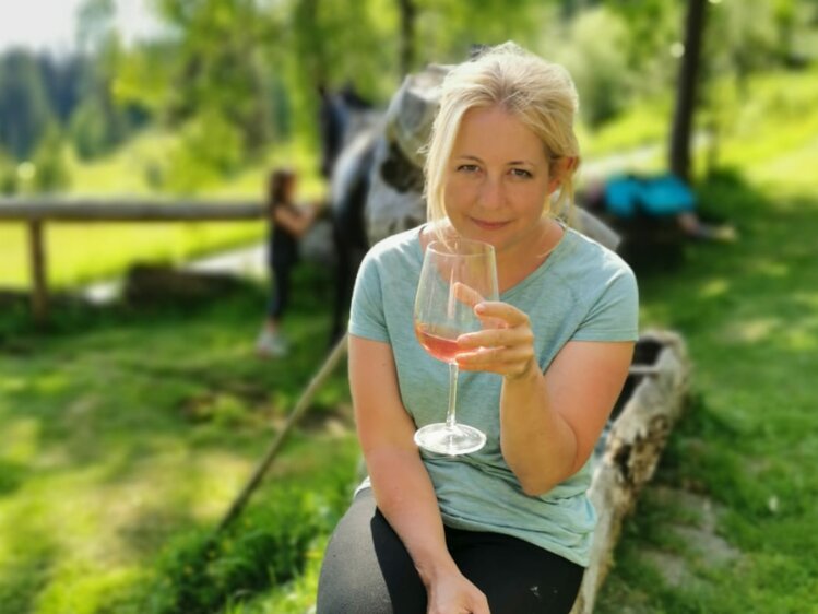 Woman in casual clothing enjoying a glass of wine outdoors amidst lush greenery and nature. | © Urlaub am Bauernhof / Schell