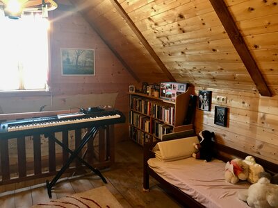 Klavier | © Urlaub am Bauernhof / Schell Cozy attic room with piano, bookshelf, and plush toys, surrounded by wooden beams and wall panels. | © Urlaub am Bauernhof / Schell