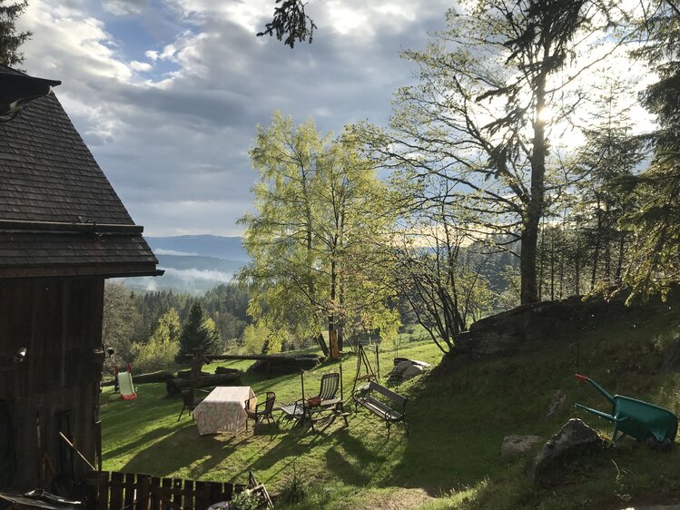 Rustic wooden cabin, lush green meadow, forest canopy, chairs and weathered furniture, scenic mountain landscape. | © Urlaub am Bauernhof / Schell