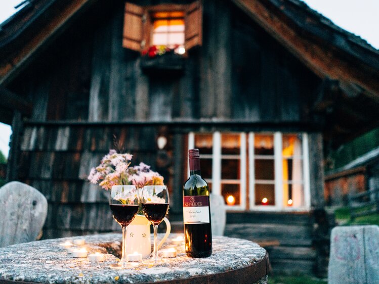 Cozy wooden cabin, warm candlelight, red wine, and floral bouquet on a rustic table, creating an inviting and charming atmosphere. | © Urlaub am Bauernhof Kärnten/ Daniel Gollner