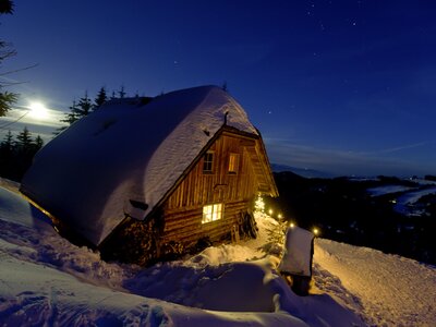Kärntner Alm bei Nacht im Winter | © Urlaub am Bauernhof/ Tom Lamm Cozy wooden cabin nestled in snowy landscape, illuminated at night under starry sky. Serene winter scene. | © Urlaub am Bauernhof/ Tom Lamm