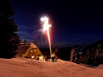 Silvester auf der Alm | © Urlaub am Bauernhof/ Tom Lamm Snowy landscape with wooden cabin, people watching fireworks display against night sky with starry background. | © Urlaub am Bauernhof/ Tom Lamm