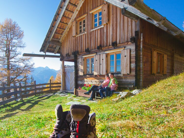 Rustic wooden mountain cabin, hikers resting on porch, snow-capped peaks in background, hiking boots in foreground.