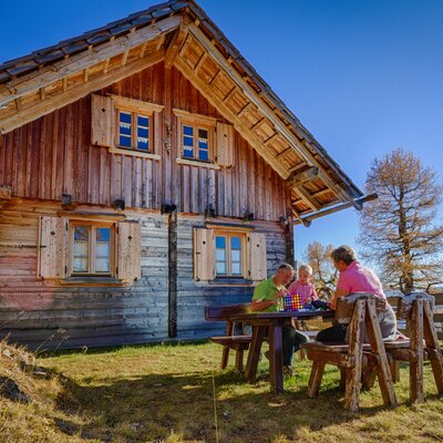 Rustic wooden cabin with family seated at table enjoying autumn landscape overlooking lake.