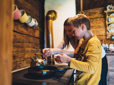 Two young people preparing food together in a rustic kitchen with wooden shelves and kitchen utensils. | © Urlaub am Bauernhof Salzburg / Daniel Gollner 