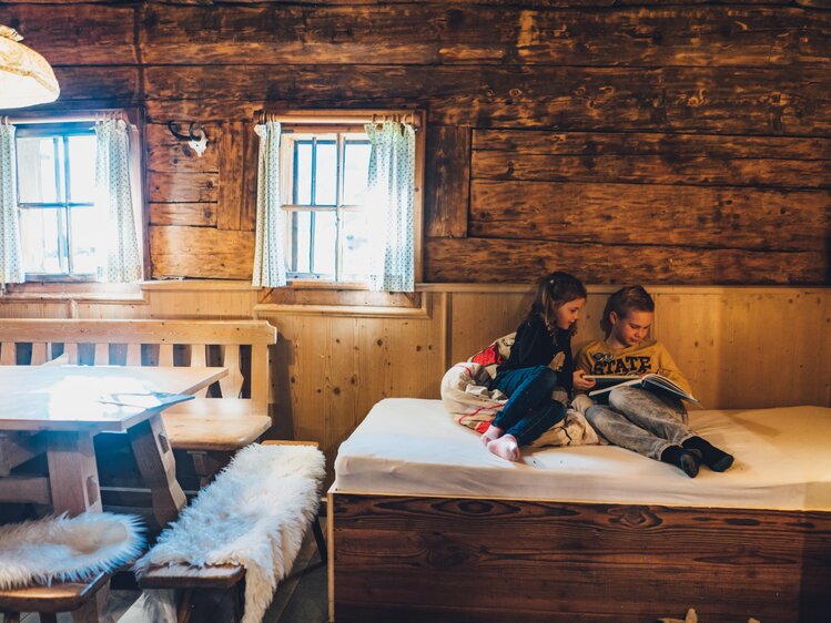Cozy wooden cabin interior with two people sitting on a bed, reading and relaxing in a rustic, intimate setting. | © Urlaub am Bauernhof Salzburg / Daniel Gollner 