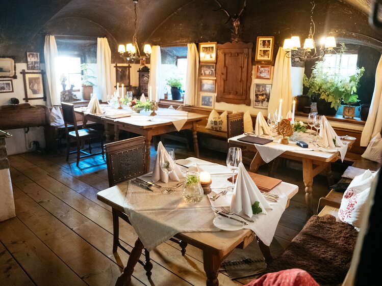 Traditional rustic dining room with wooden furniture, candelabras, and décor items, creating a cozy and inviting atmosphere. | © Urlaub am Bauernhof / Daniel Gollner