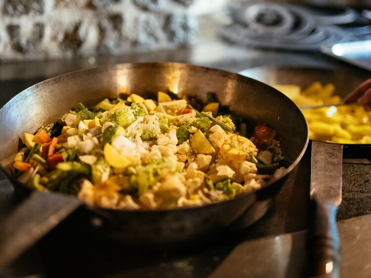 Sizzling pan containing a colorful mix of vegetables, potatoes, and what appears to be chicken or turkey pieces, creating an appetizing meal. | © Urlaub am Bauernhof / Daniel Gollner