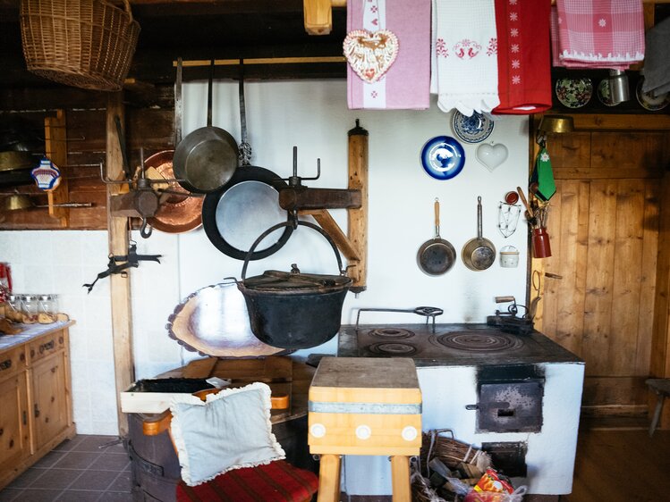 Rustic kitchen with antique cookware, wooden furniture, and decorative elements such as heart-shaped ornaments and patterned textiles. | © Urlaub am Bauernhof / Daniel Gollner