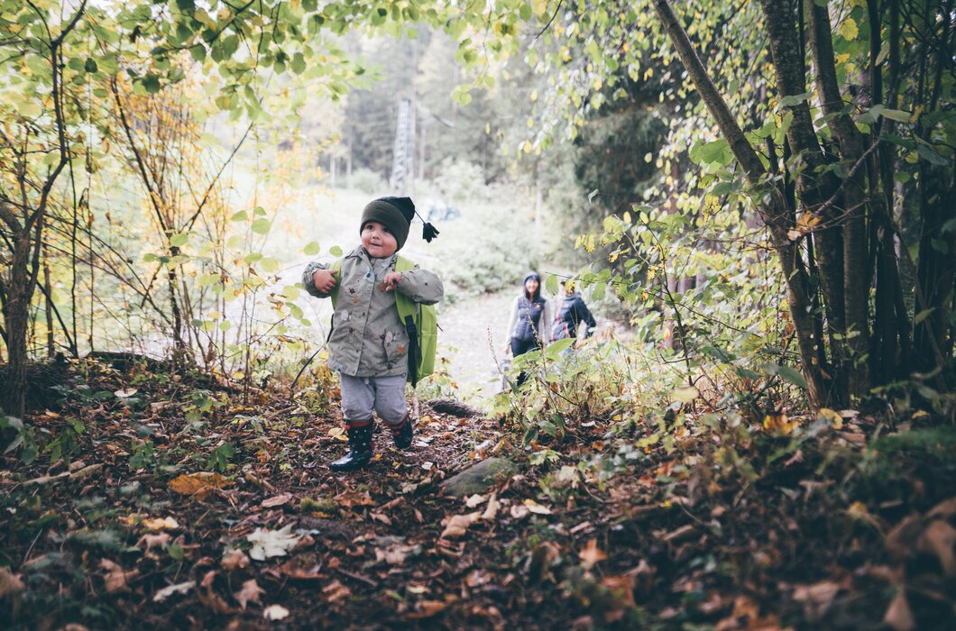 A small child in casual autumn attire exploring a lush, wooded path, with two adults walking behind in the distance. | © Urlaub am Bauernhof / Daniel Gollner
