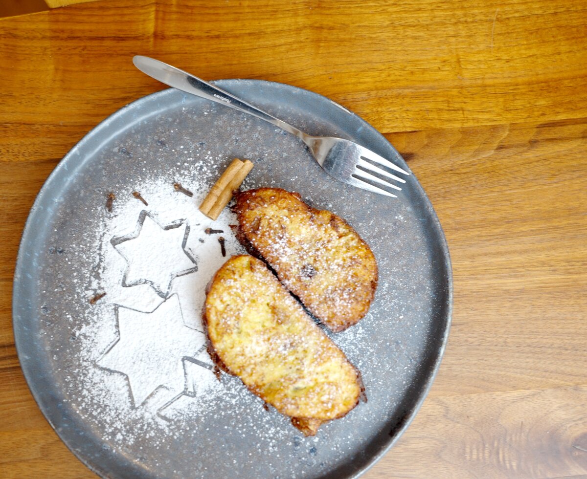 Plate with fried pastries dusted with powdered sugar, a fork, and decorative star-shaped cutouts on a wooden table. | © Urlaub am Bauernhof / Daniel Gollner