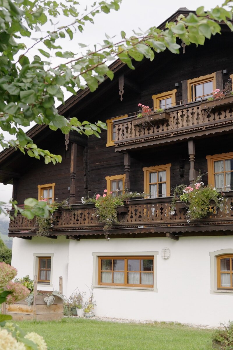 Quaint alpine-style wooden chalet with ornate balconies, surrounded by lush greenery and flowers. | © Urlaub am Bauernhof / Daniel Gollner