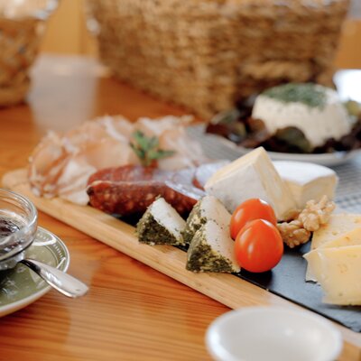Gedeckter Tisch | © Urlaub am Bauernhof / Daniel Gollner Assortment of meats, cheeses, breads, and condiments on a wooden board, a traditional European-style charcuterie platter. | © Urlaub am Bauernhof / Daniel Gollner