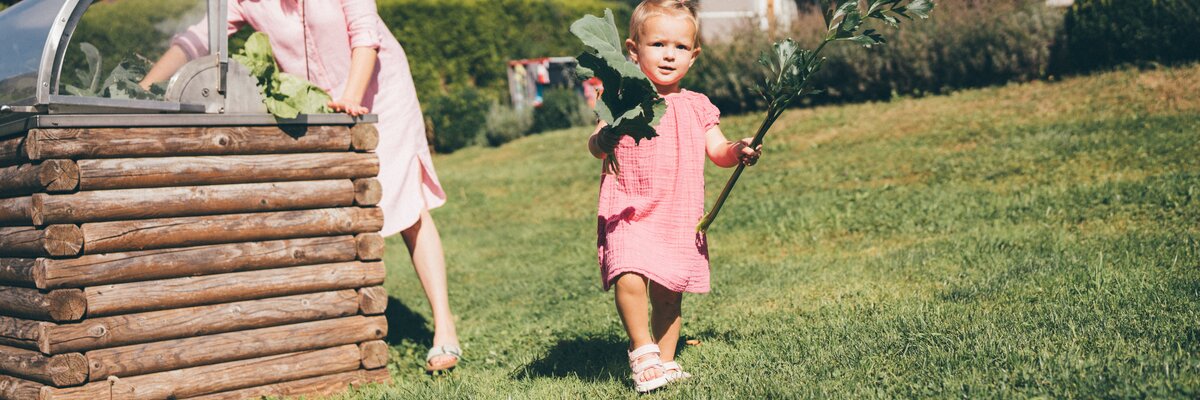 Young woman and child playing in a garden with a wooden crate, enjoying the outdoors on a sunny day. | © Urlaub am Bauernhof / Daniel Gollner