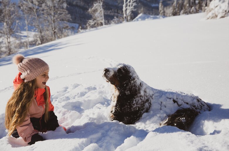 Mädchen mit Hund im Schnee | © Urlaub am Bauernhof / Pascal Baronit Young girl playing with large black dog in snowy winter landscape. | © Urlaub am Bauernhof / Pascal Baronit
