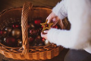 Wicker basket filled with ornate Christmas ornaments, including a golden star, held by a hand in a white furry cuff. | © Urlaub am Bauernhof / Pascal Baronit