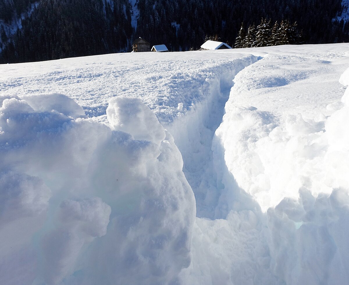Thick snow covers the ground and slopes, with a cleared path through the snowy landscape and small buildings visible in the distance. | © Urlaub am Bauernhof / Markus Lackinger