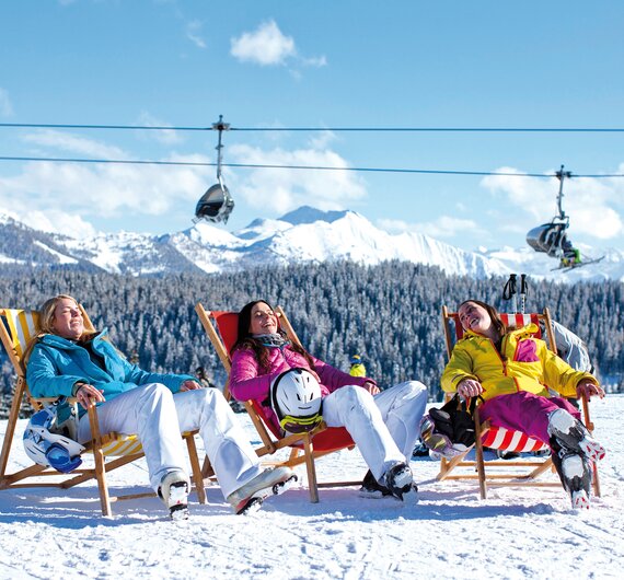 Entspannt Sonne tanken auf der Piste, Salzburger Sportwelt | © Salzburger Sportwelt  Drei Skifahrerinnen genießen die Sonne in Sonnenliegen auf der Piste, im Hintergrund Sessellift, Salzburger Sportwelt | © Salzburger Sportwelt