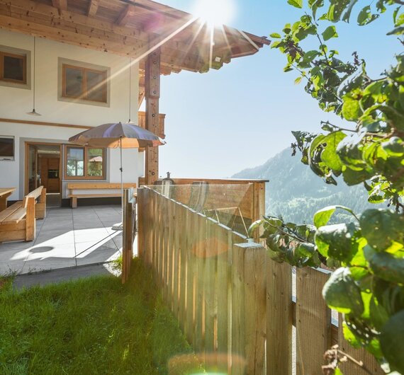 The farmhouse's outdoor terrace includes wooden seating, a sun umbrella, and mountain views.
