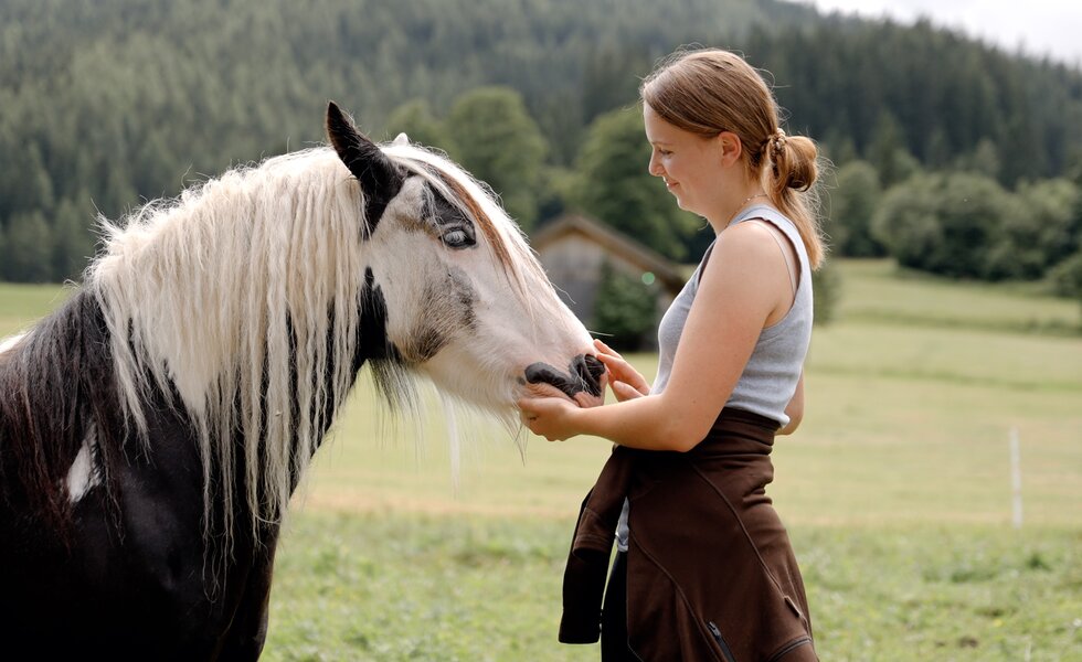 Bäuerin streichelt liebevoll ein Pferd auf einer grünen Weide | © Urlaub am Bauernhof Steiermark / Daniel Gollner