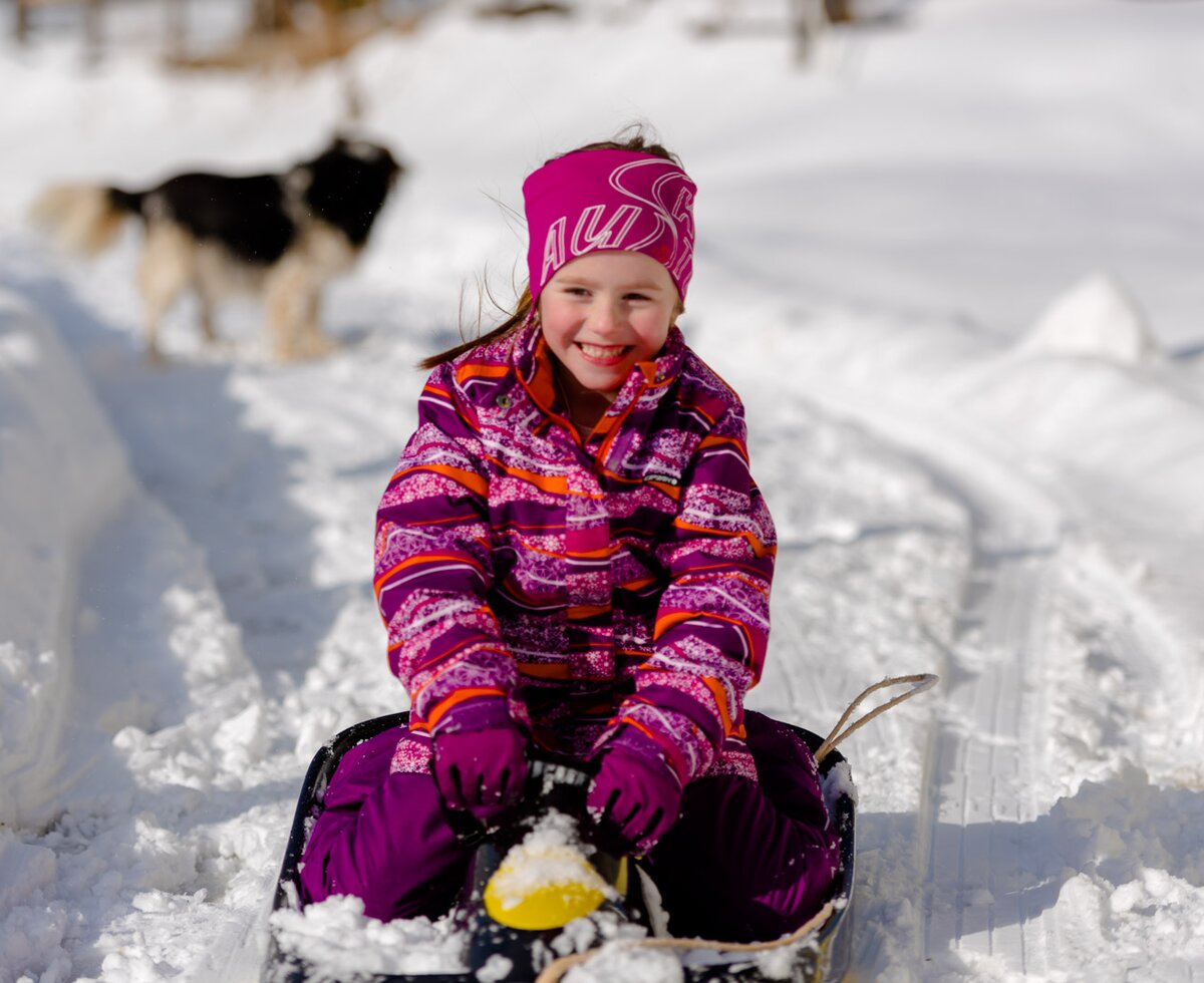 Kind beim Bobfahren mit Hund im HIntergrund, Urlaubsregion Murau-Murtal, Steiermark | © Urlaub am Bauernhof Steiermark / Wolfgang Spekner