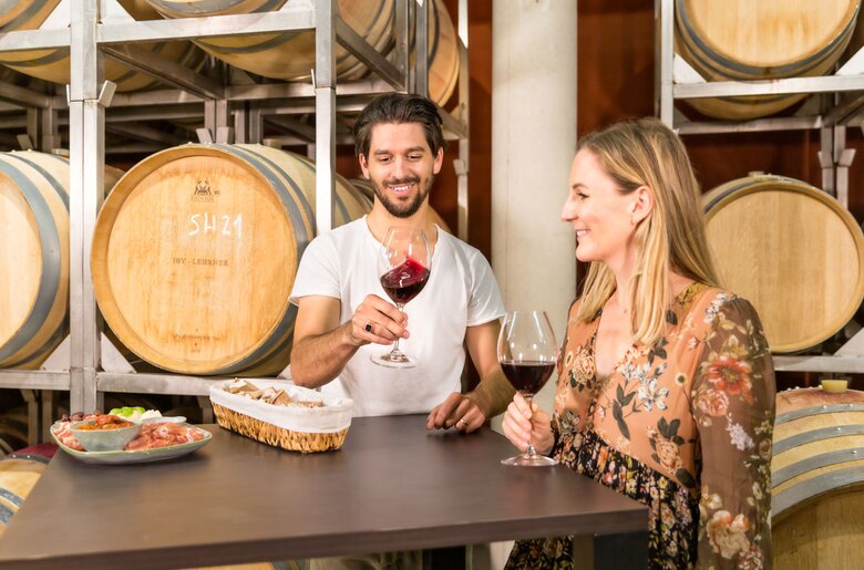 A happy couple enjoying a wine tasting in a cellar surrounded by oak barrels and wooden crates, sharing a casual moment together.