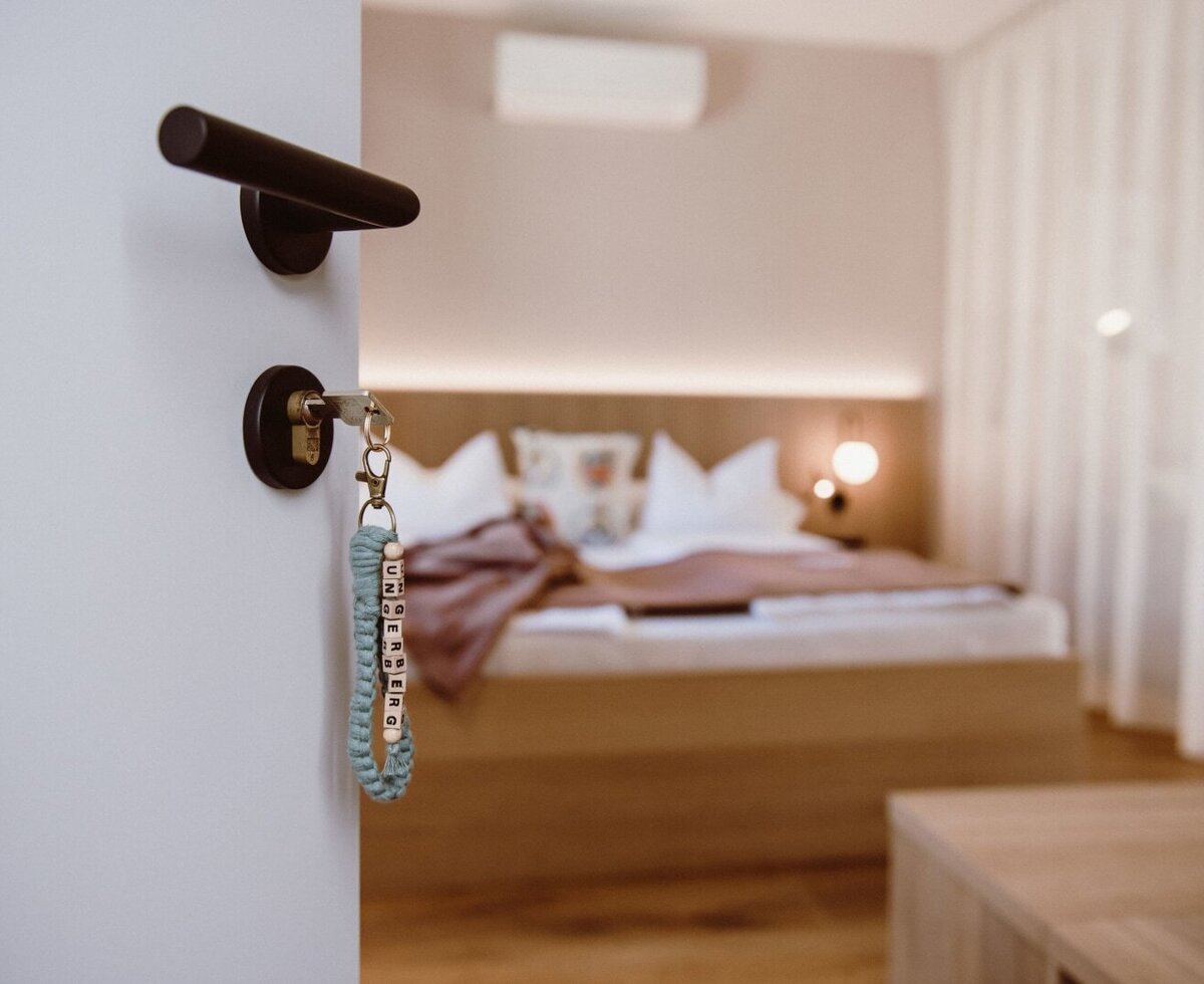 The bedroom at the farmhouse, shown from the doorway with key, features a wooden bed frame, integrated backlighting, and air conditioning.