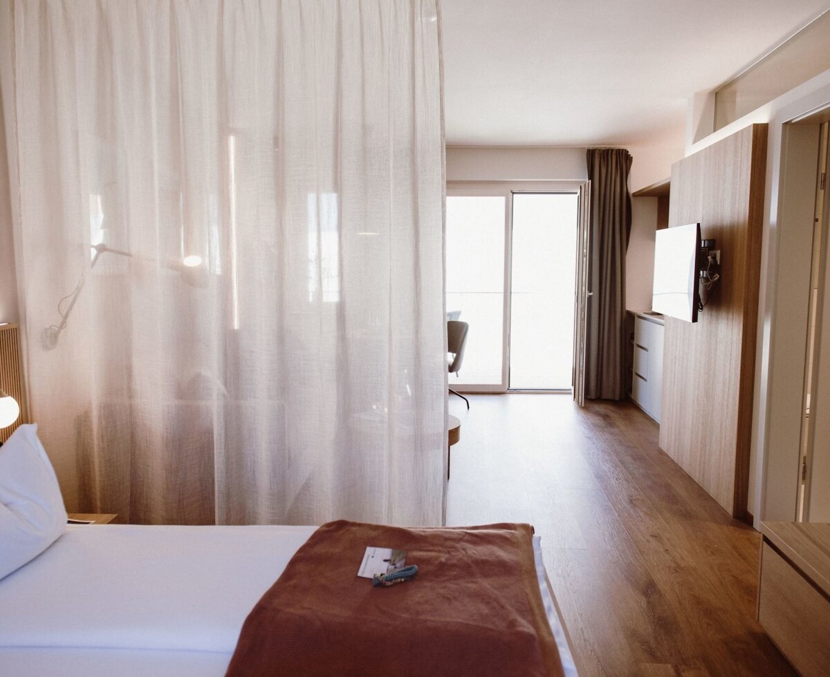 A room in the farmhouse featuring a bed, a sheer curtain room divider, a TV mounted on a wooden panel, and a sliding door leading to a balcony.