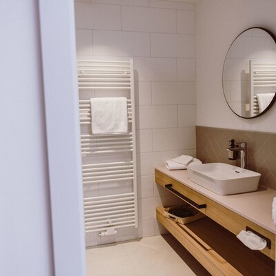 The farmhouse bathroom is equipped with a towel warmer, a modern sink on a wooden vanity with storage, and a round mirror.