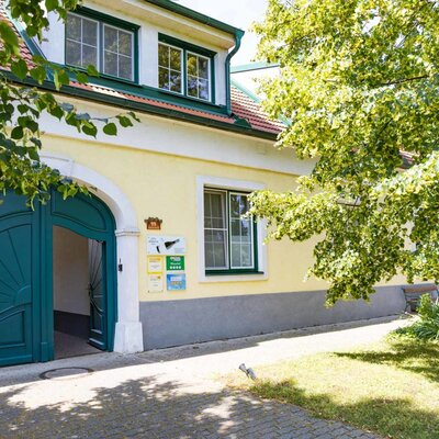Entrance to the house, featuring large green wooden doors and information signs on the facade.