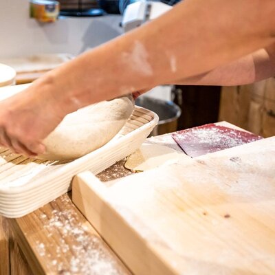 Hands preparing bread dough in a proofing basket on a wooden counter at the farm house.