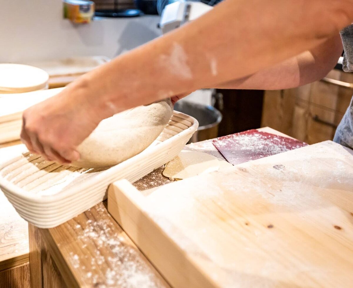 Hands preparing bread dough in a proofing basket on a wooden counter at the farm house.