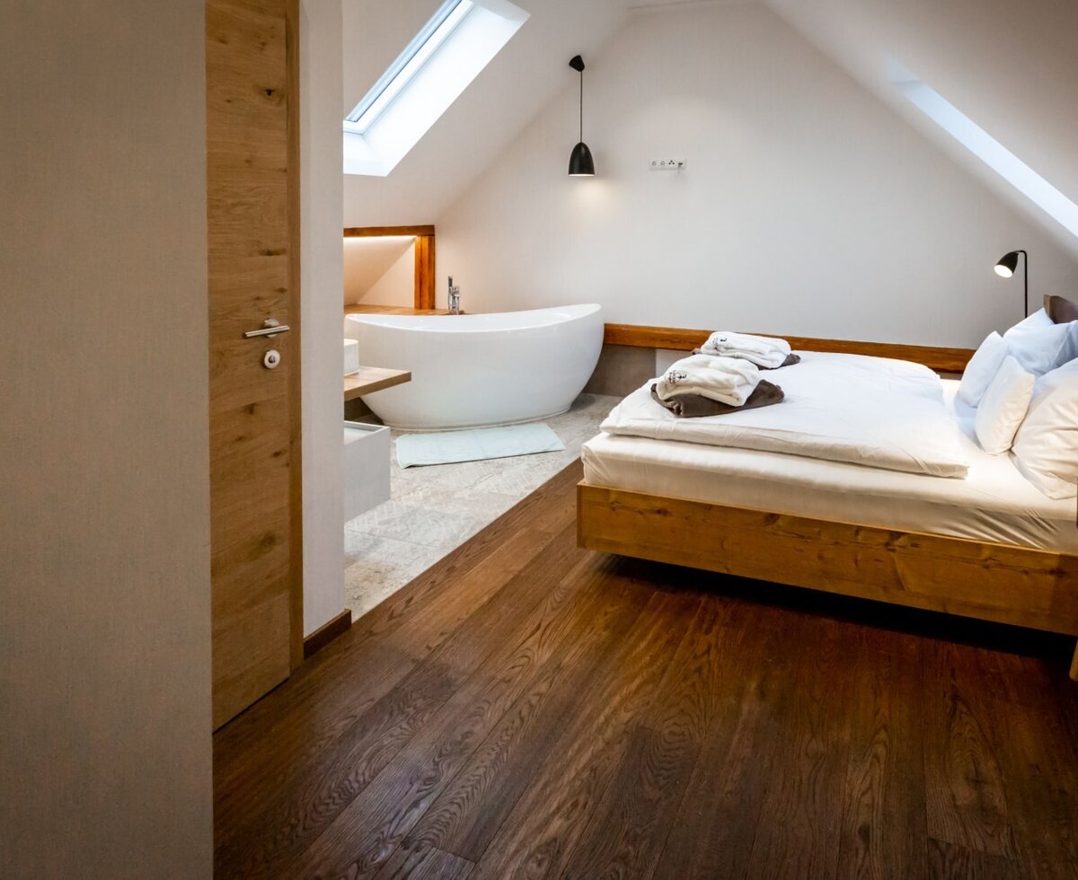 The Farm House offers a bedroom area with a double bed and an adjacent freestanding bathtub, illuminated by a skylight.