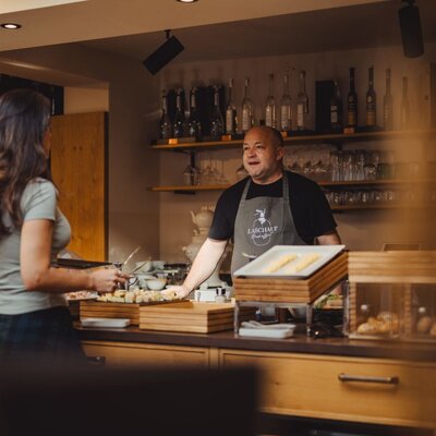 The host at the farmhouse breakfast buffet, speaking with a guest.