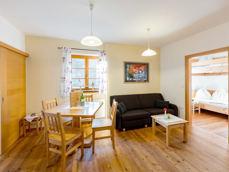 Living area in the farmhouse featuring a dining table, sofa, wooden floor, and an adjacent bedroom with bunk beds.