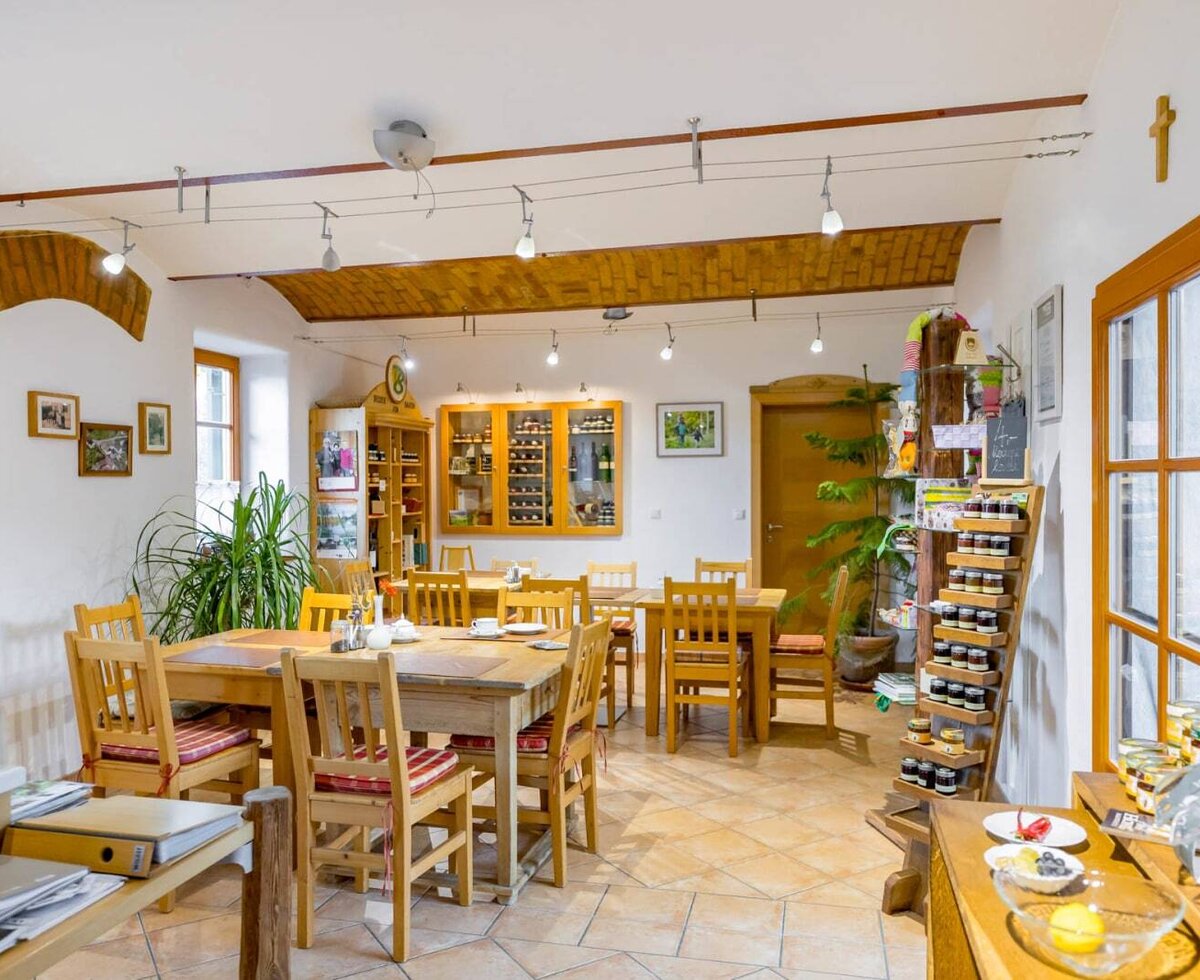 The dining area of the farmhouse with wooden tables, chairs, tiled floor, and a shelf with local products.