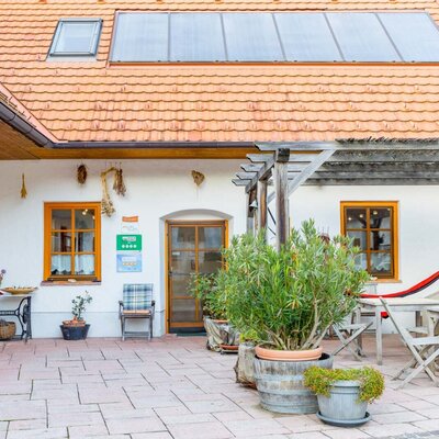 The outdoor terrace of the farmhouse with seating, a hammock under a wooden pergola, and solar panels on the tiled roof.