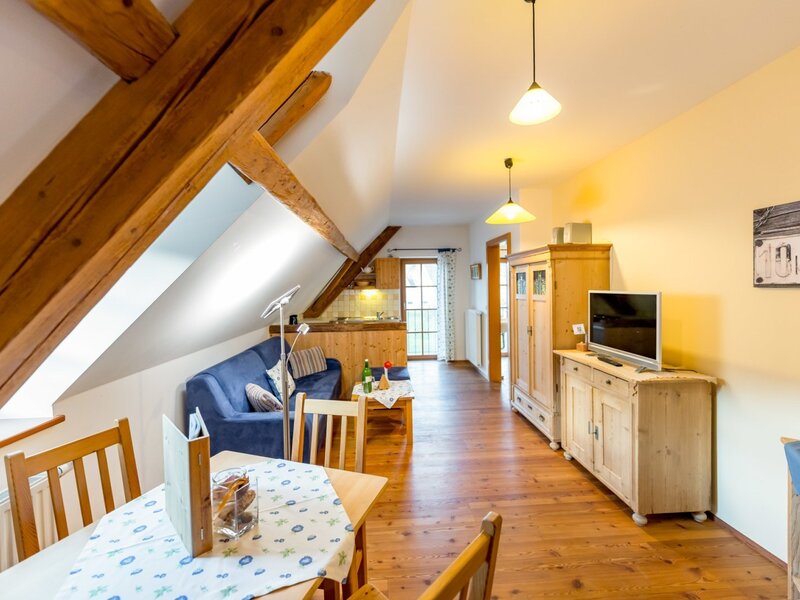 Spacious living area in the farmhouse with a dining table, sofa, kitchenette, exposed wooden beams, and wooden floor.