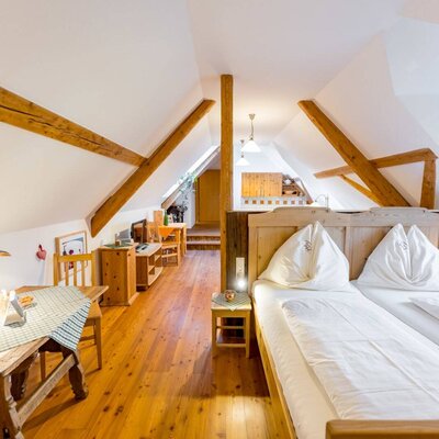 Attic bedroom in the farmhouse with a double bed, wooden floor, exposed wooden beams, and a separate dining area.