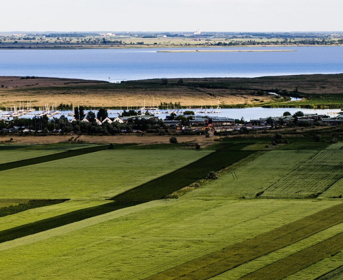 View from the farmhouse of green agricultural fields, a lake with a marina, and a distant coastline.