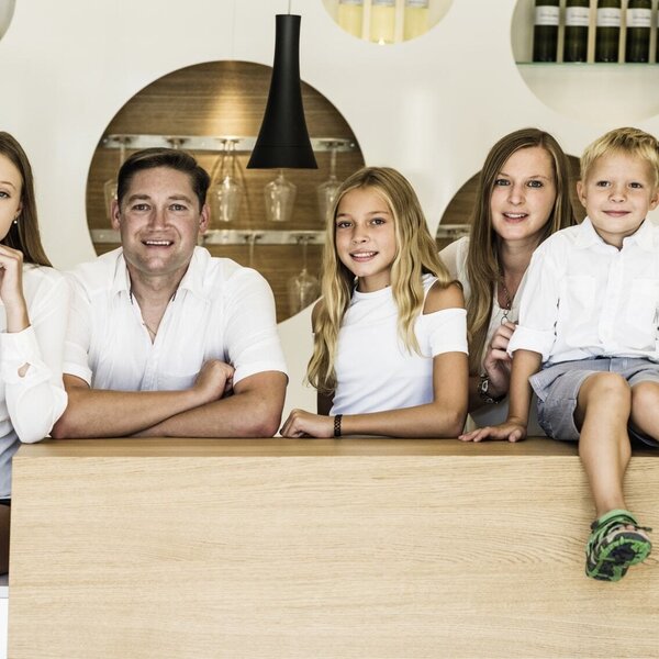 The family who operates the farmhouse, standing behind a wooden counter with wine bottles and glassware on display.